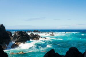 ocean waves crashing on rocks under blue sky during daytime